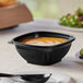 A Visions black plastic square bowl filled with soup on a table.