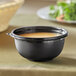 A black Visions plastic bowl of soup on a table.