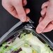 A person using a knife to cut salad in a Sabert clear plastic bowl on a counter.