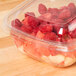 A Sabert clear plastic square bowl filled with raspberries and fruit with a clear lid.