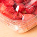 A Sabert clear plastic square bowl filled with raspberries and strawberries.