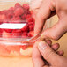 A person cutting up raspberries into a Sabert SureStrip plastic container on a counter.