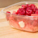 A Sabert clear plastic bowl filled with raspberries and strawberries on a wood surface.