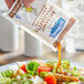 A person pouring Hellmann's Balsamic Vinaigrette dressing from a packet onto a salad.