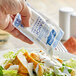 A hand pouring Hellmann's Light Ranch Dressing from a packet onto a salad.