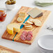 An American Metalcraft rectangular olive wood serving board with blue polyresin streaks holding cheese, crackers, and green olives.