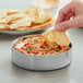 A hand holding a chip and dipping it into a stainless steel bowl of dip.