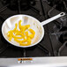 A Vollrath Arkadia aluminum frying pan with yellow peppers in it.