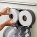 A person putting a Lavex Premium 2-ply jumbo toilet paper roll into a toilet paper holder.