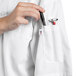 A person putting a pen in the pocket of a white Uncommon Chef Aruba Pro Vent chef coat.