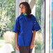 A woman wearing a Uncommon Chef royal blue short sleeve chef coat.