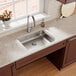 An Elkay stainless steel single bowl undermount sink with a Perfect Drain on a kitchen counter in front of a window.