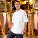 A man in a white Uncommon Chef Delray Pro Vent chef coat standing in front of a large copper kettle.