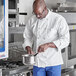 A man in a white Uncommon Chef long sleeve coat cooking in a professional kitchen.