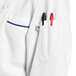 A white Uncommon Chef long sleeve chef coat with royal blue piping on the counter with three pens in the pocket.
