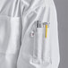 A person wearing a Uncommon Chef white long sleeve chef coat with a yellow pen in the pocket.