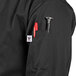 A person wearing a black Uncommon Chef Rio long sleeve chef coat with a red pen in the pocket.