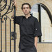 A man wearing a black Uncommon Chef Antigua Pro Vent short sleeve chef coat with a mesh back.