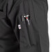 A black Uncommon Chef Aruba Pro Vent chef coat with a pocket and pen holder.