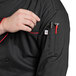 A person wearing a black Uncommon Chef Murano chef coat with red piping and a pen in the pocket.