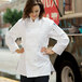 A woman wearing a Uncommon Chef white long sleeve chef coat standing in a professional kitchen.