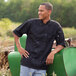 A man wearing a black Uncommon Chef Montego Pro Vent short sleeve chef coat with mesh back.