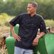 A man wearing a Uncommon Chef black short sleeve chef coat with mesh back.