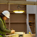 A woman in a hard hat using a Lind Equipment Beacon120 LED work light to write on a piece of wood.