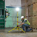 A man in a safety vest and white hard hat using a Lind Equipment Beacon360 LED area light on a tripod.