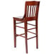 A Lancaster Table & Seating mahogany wood school house bar stool with a backrest.