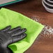 A gloved hand using a green Lavex microfiber cloth to clean a table.