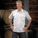 A man in a white Mercer Culinary short sleeve work shirt standing in front of barrels.