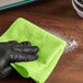 A hand in a black glove wiping a green Lavex microfiber cloth.