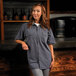A woman standing in a professional kitchen wearing a gray Mercer Culinary short sleeve work shirt.
