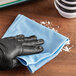 A hand in a black glove wiping a blue Lavex microfiber cloth.