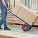 A person in blue jeans pushing a Lavex blue hand truck with boxes.