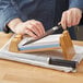 A person using a Shun knife to cut paper on a wooden cutting board.