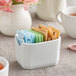 A white Tuxton rectangular china container holding sugar packets on a counter.