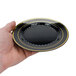 A hand holding a Fineline black plastic plate with a gold rim.
