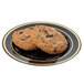 A Fineline black plastic plate with a gold band holding two chocolate chip cookies.