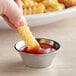 A hand holding a french fry in a American Metalcraft stainless steel sauce cup filled with ketchup.