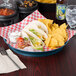 A blue polypropylene round deli server on a table with a plate of tacos and chips.