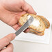 A person spreading butter on a piece of bread with a Vollrath Queen Anne stainless steel butter knife.