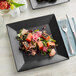 A piece of salmon, salad, and vegetables on a black Acopa stoneware plate.