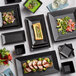 A table set with Acopa matte black square stoneware plates of food including a bowl of green soup.