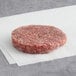 A Warrington Farm Meats frozen raw burger patty on a white napkin.