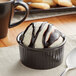 A glossy black Acopa fluted stoneware ramekin filled with ice cream drizzled with chocolate sauce with a spoon next to it.