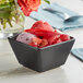 A matte black Acopa stoneware bouillon bowl filled with fruit ice cream and grapes.