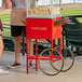 A man standing next to a red cart with a Carnival King popcorn machine.