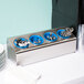 A silver Steril-Sil countertop organizer with blue lids and silver spoons inside.
